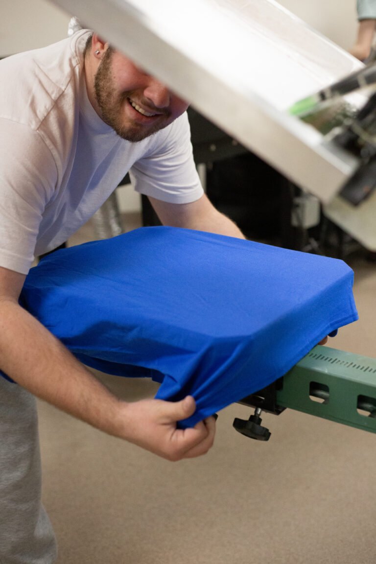 Screen printer inspecting a blue T-shirt on a printing press